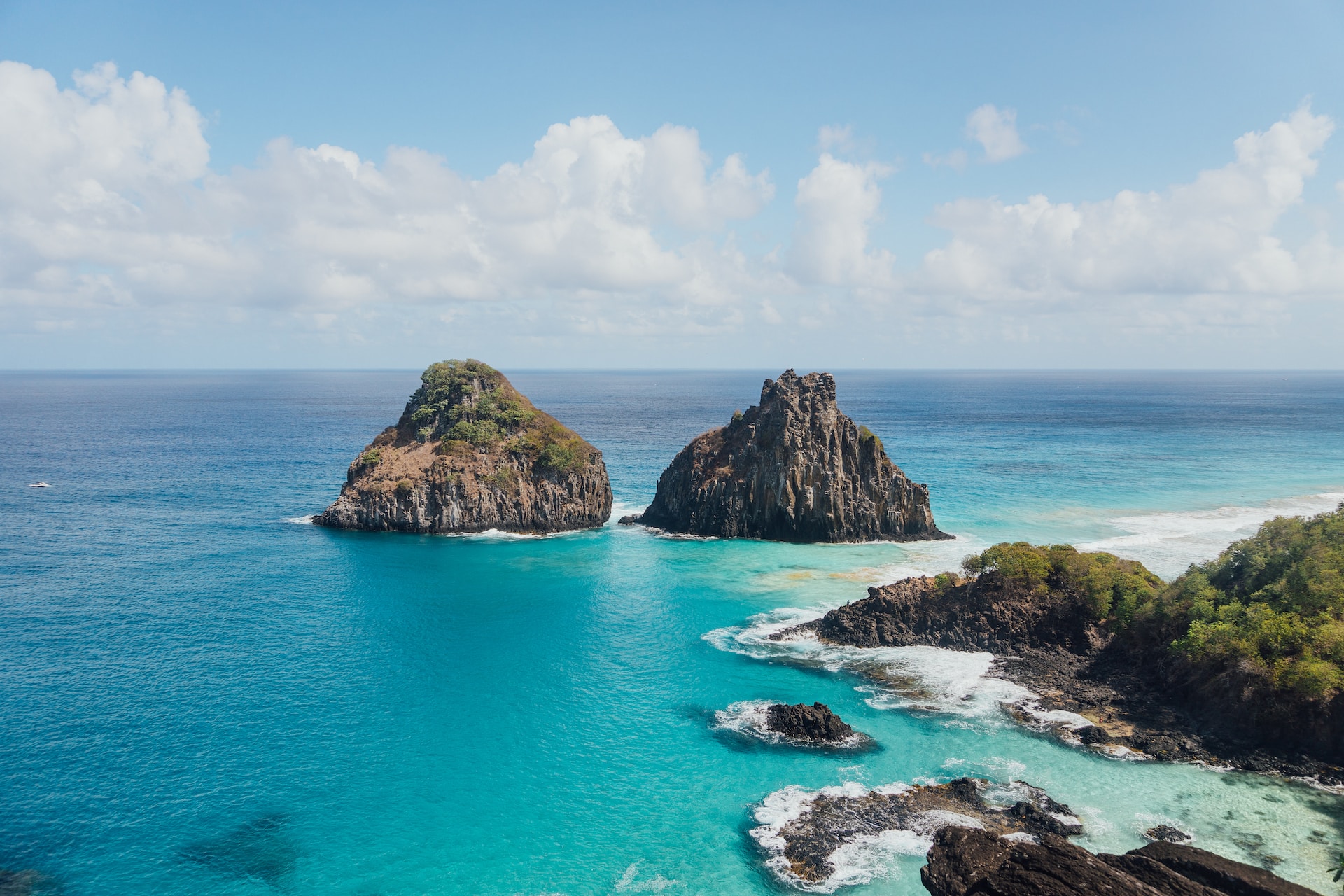 Brown and green rock formation on blue sea under white clouds and blue sky during the day
