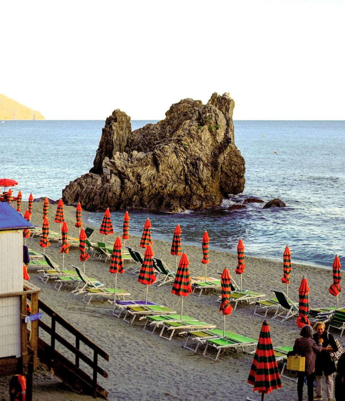 Cinque Terre in April can be a little cool, especially when it comes to the sea temperatures. But, there's still plenty to do and enjoy at the start of spring! View of Monterosso al Mare beach with closed umbrellas and a large rock along the sea shore.