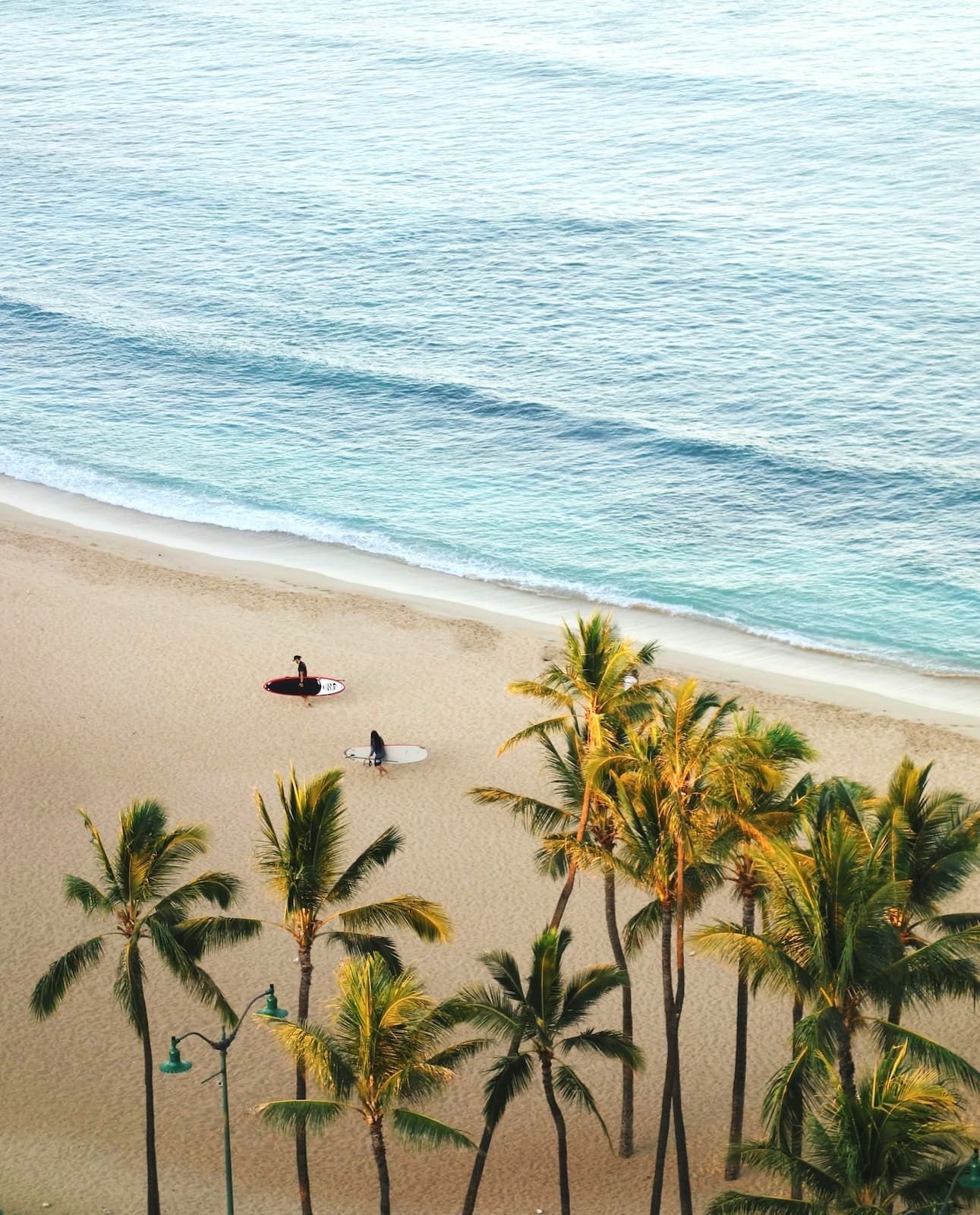 Oahu has some of Hawaii's best beaches Two people carrying surfboards at sunset on Queen's Beach, Oahu